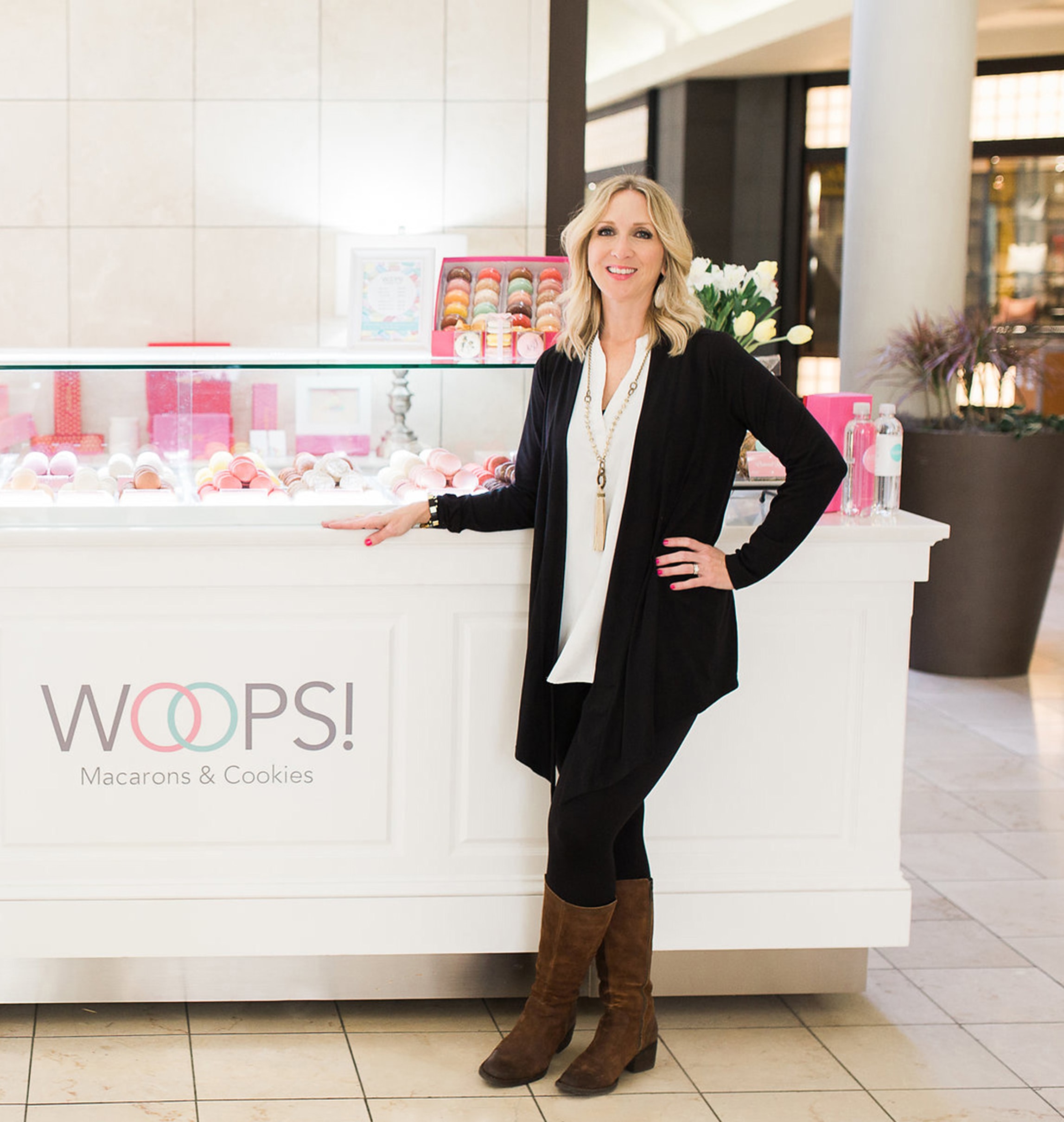 Owner of Woops! French Macaron Franchisee with the macaron counter and some flowers at the back
