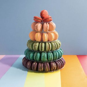 A French macaron pyramid with assorted flavors is standing on top of a rainbow-colored base.