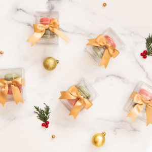 Several macaron favor boxes are surrounded by Christmas ornaments.