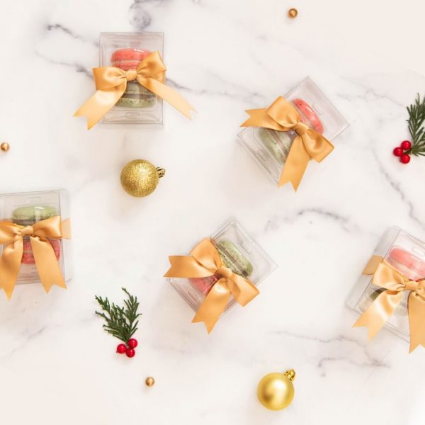 Several macaron favor boxes are surrounded by Christmas ornaments.