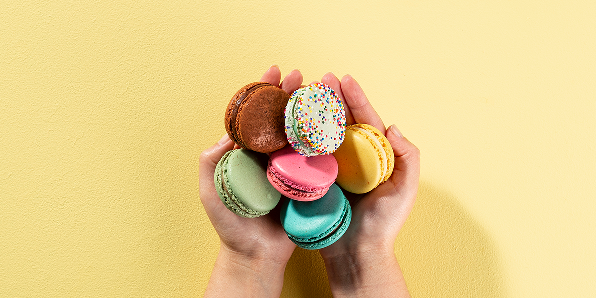 Hand holding Woops! macarons with a yellow background