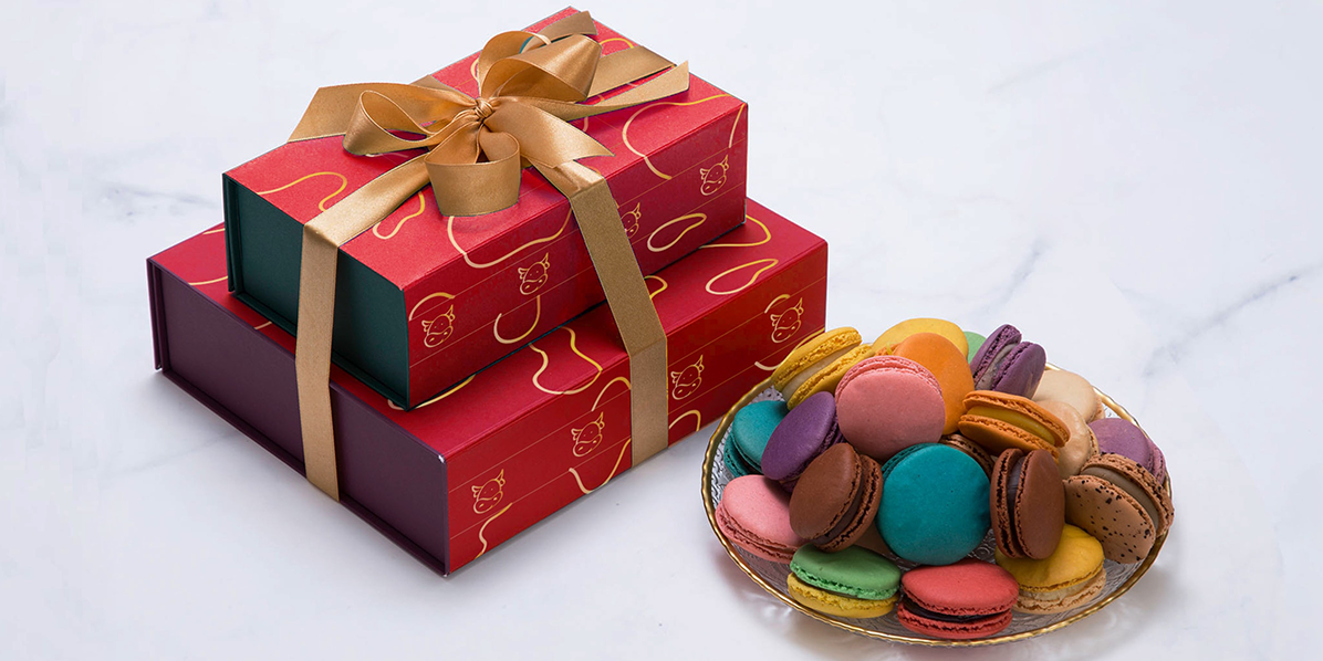 Stack of a macarons with an assorted box of 9 and 18 with a ribbon on top. Each box packaged with a Lunar New Year sleeve