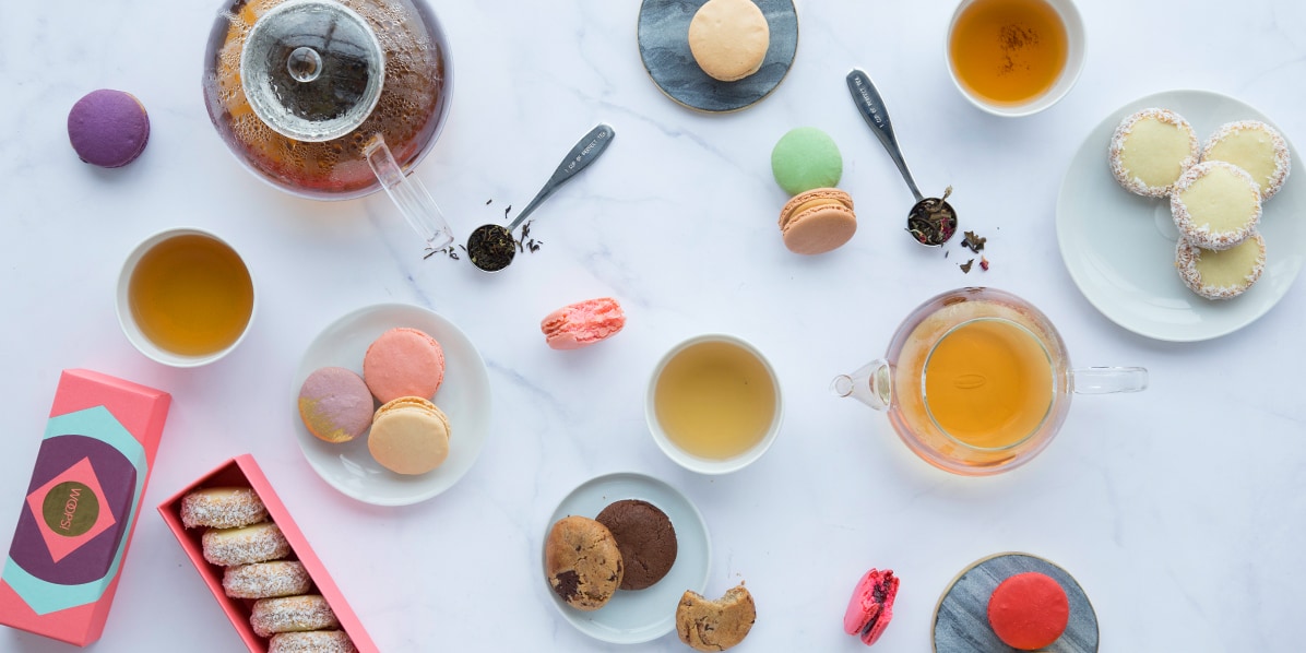 Assortment of macaron flavors, alfajores, and cookies with teapots & teacups