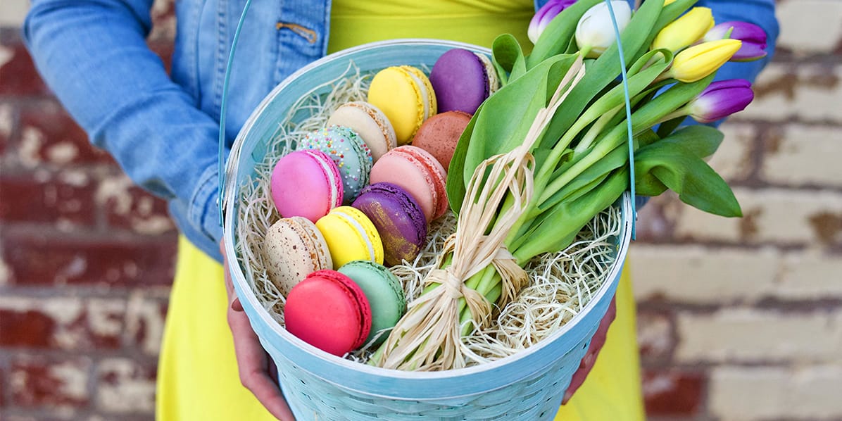 Basket full of an assortment of macarons and flowers on the lap of a woman with a green dress