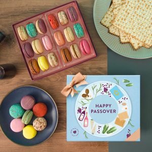 Colorful macarons in an open box and on a plate beside a “Happy Passover” macaron gift box and matzo crackers on a wooden table.