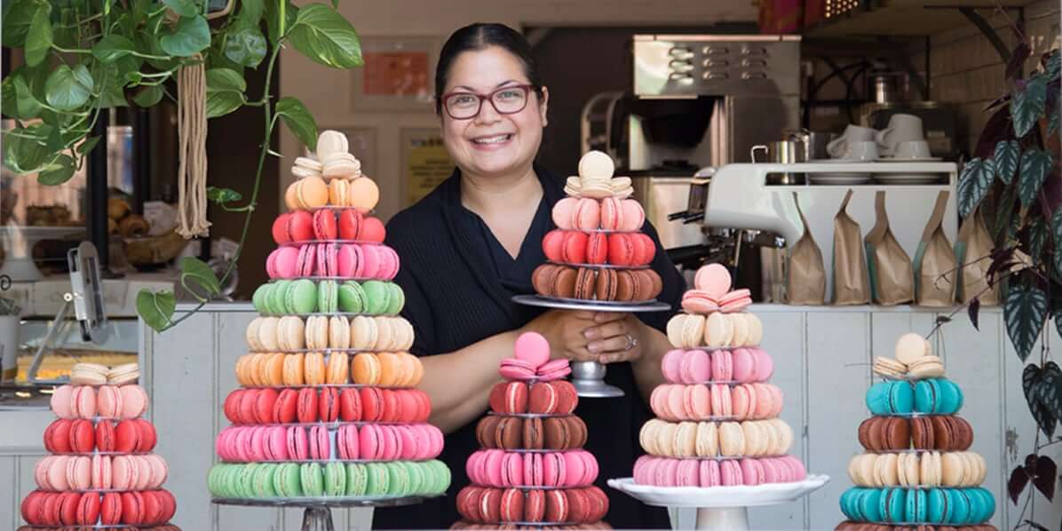 Woman smiling at a Woops! bakeshop window with macaron pyramids around