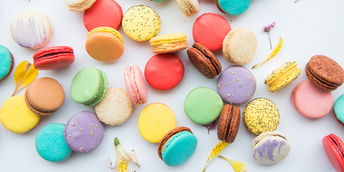 Assortment of macarons in a white background surrounded by little flowers and petals.