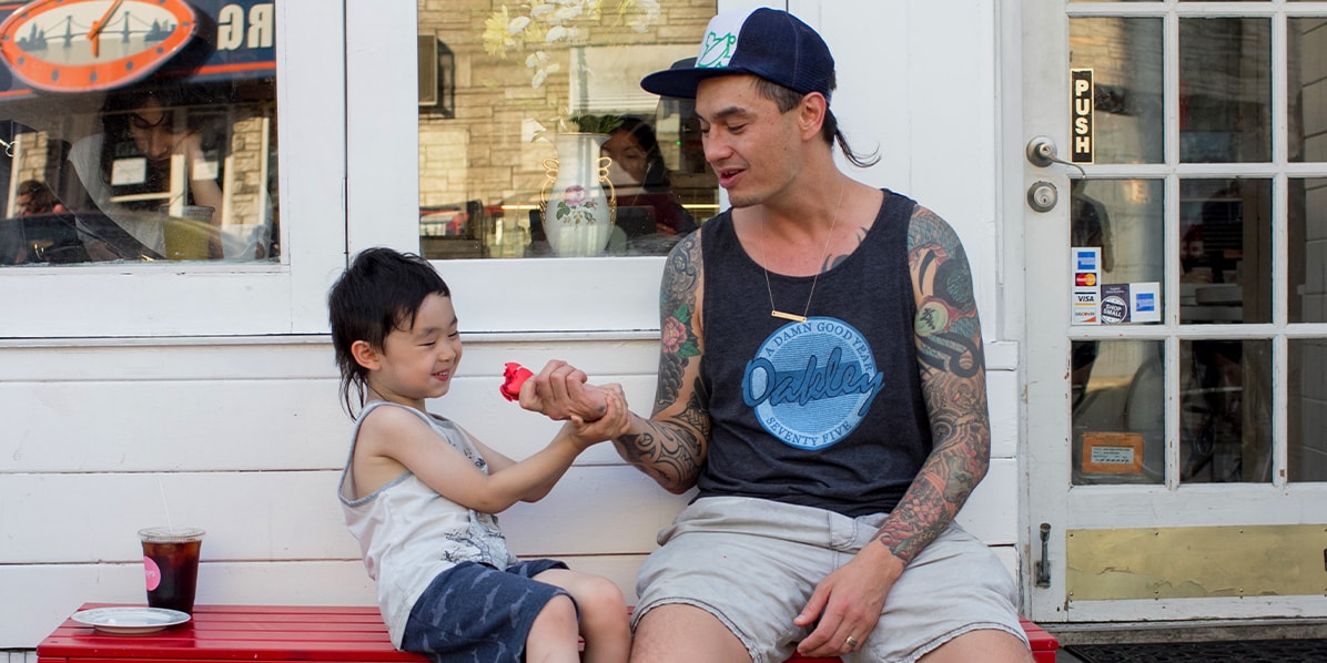 A man with his little son sharing a French macaron while sitting on a bench outside of a Woops! Bakeshop