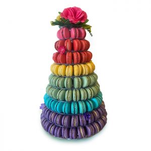 A white background features a large-sized French macarons pyramid with a rainbow color pattern that has a big red flower at the top.