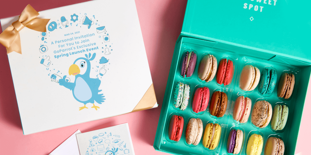 An opened French macaron box with assorted flavors has a white and blue custom greeting card to its left.
