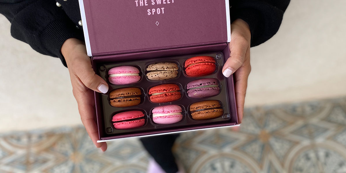 A woman is holding a box of 9 French macarons with assorted flavors.