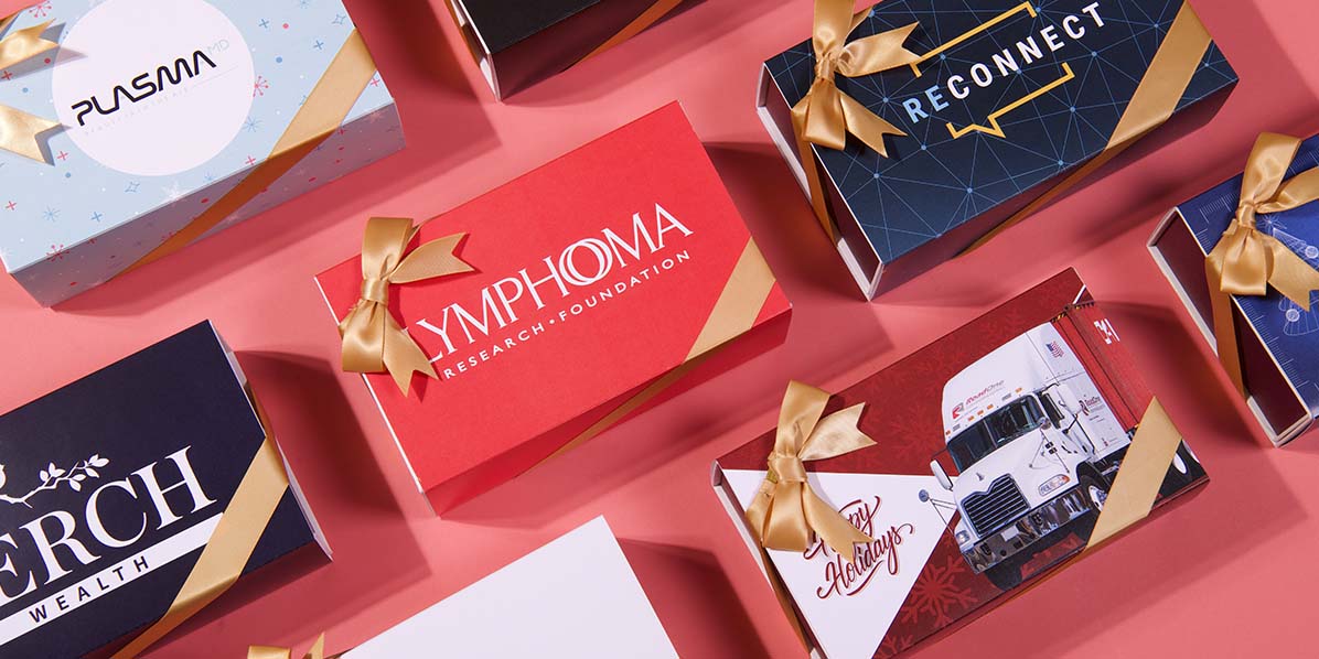 Several customized French macaron boxes with gold ribbons are lying on top of a red background