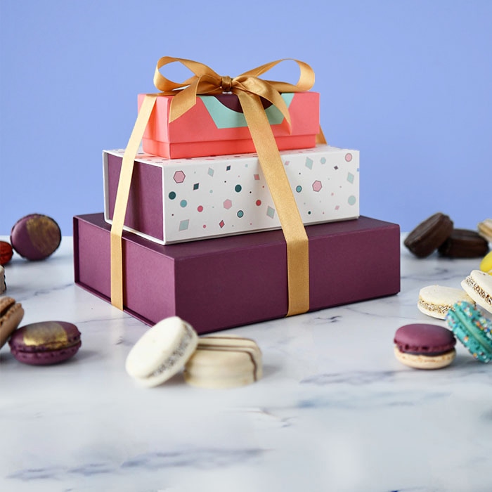 A box of 3 and 18 French macaron box with an Argentinian alfajores box stacked up with a gold ribbon holding them together, and some assorted French macarons and alfajores lying around