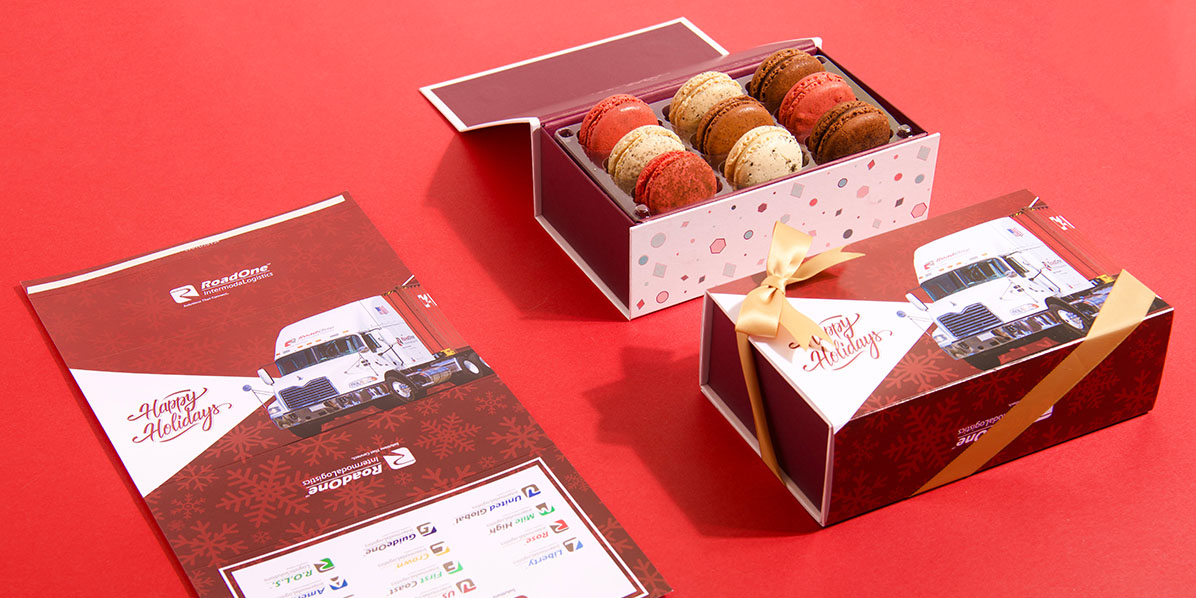 An opened and a closed box of assorted French macarons with a sleeve on the side with a logo on it