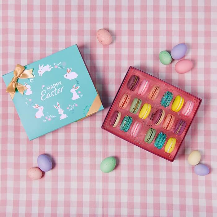 A box of 18 French macarons with assorted flavors has another box with an Easter sleeve and some colored eggs around