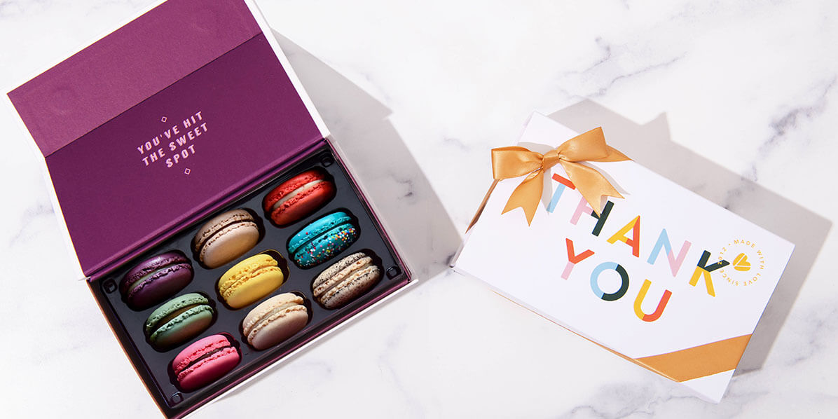 A box with 9 assorted French macarons has a French macaron box with a Thank You sleeve to the right.