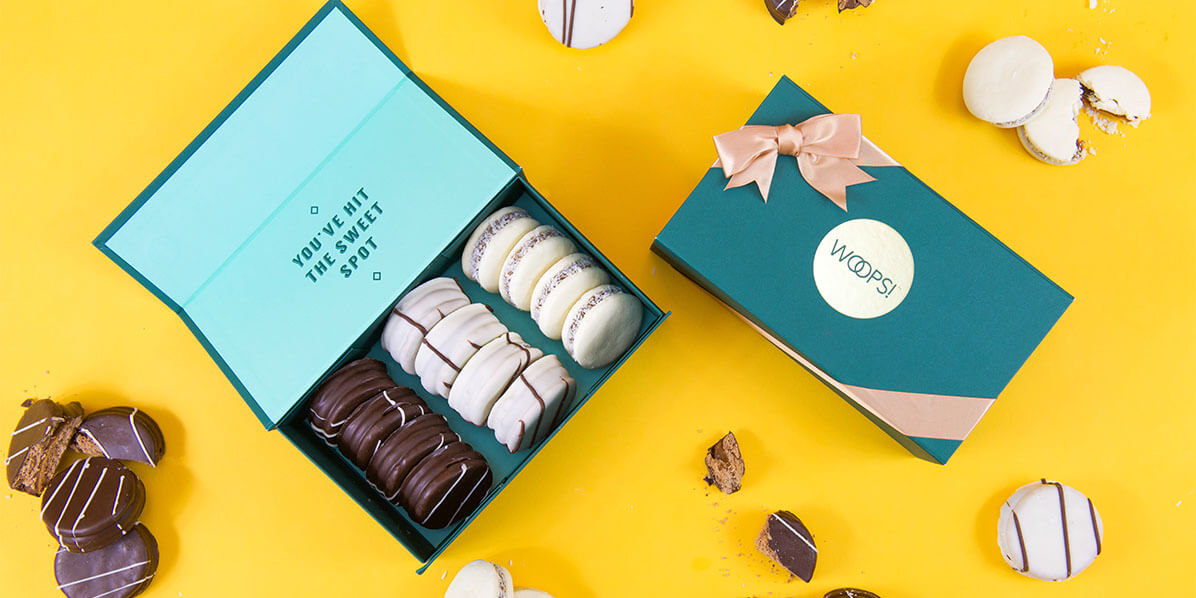 A box full of 12 assorted alfajores is surrounded by a French macaron box and assorted alfajores.
