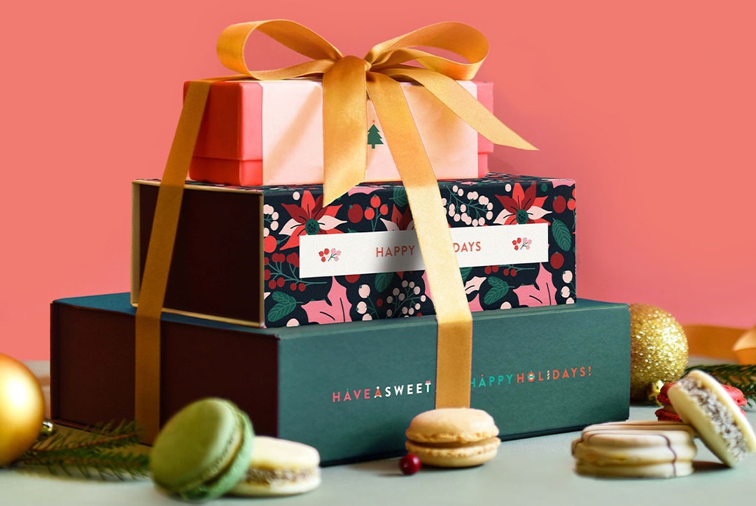 Macaron and alfajores stack with a box of 3, a box of 9 and a box of 18, packaged with Holidays sleeves and a ribbon on top holding them all together