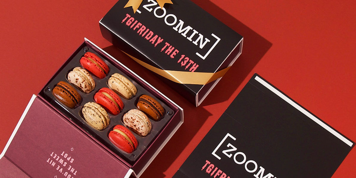 A box full of 9 assorted French macarons has a French macaron and a customized sleeve to its sides.