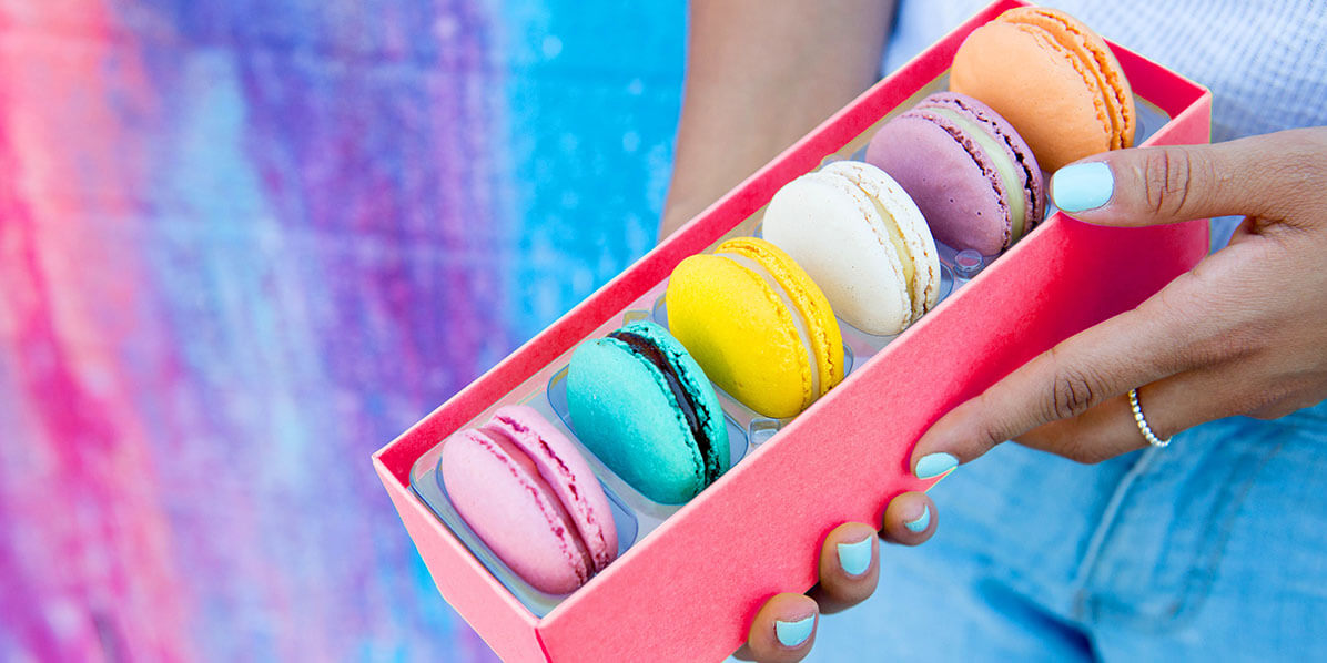 Two female hands are holding a box full of 6 assorted French macarons.