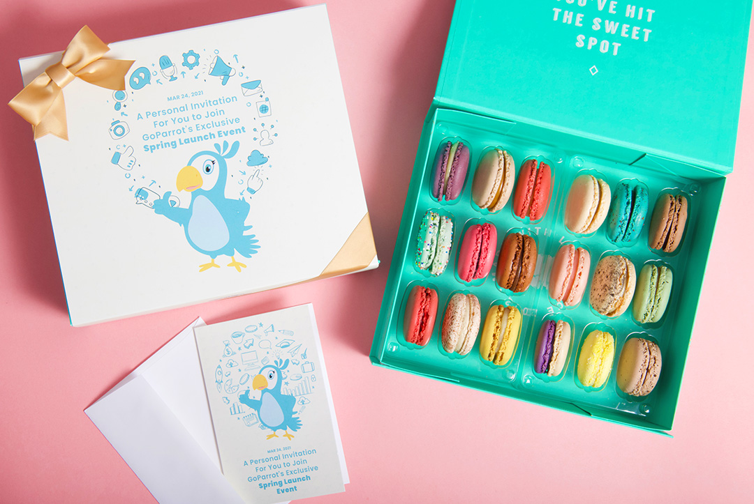 An opened French macaron box with assorted flavors has a white and blue custom greeting card.