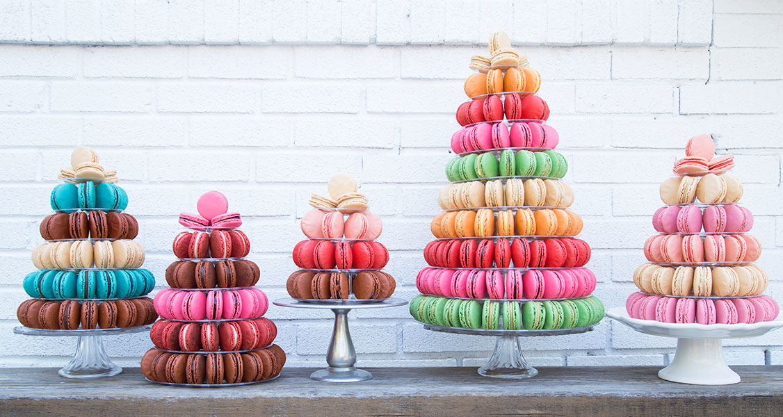 5 French macaron pyramids with assorted flavors are on top of a wooden table.