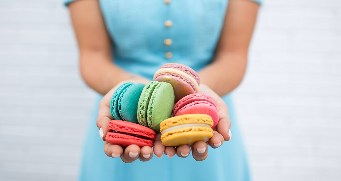 A woman with a blue dress is holding several assorted French macarons in her hands.