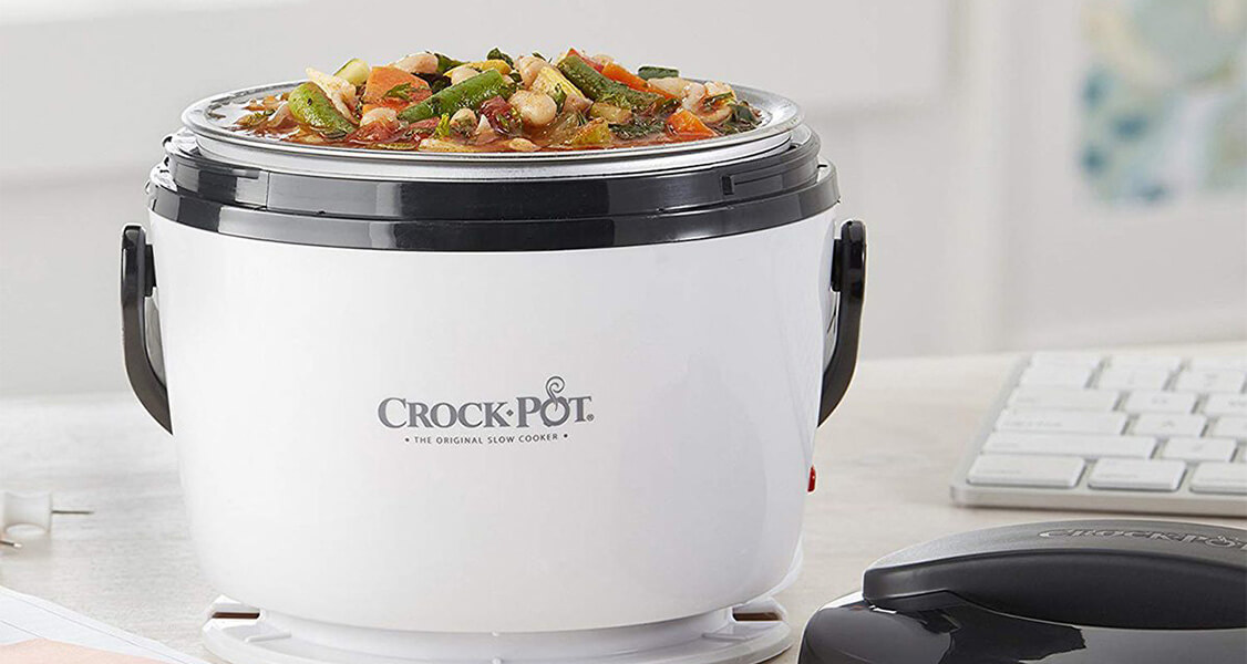 A black and white Crock Pot full of food has a keyboard and the lid to its right.