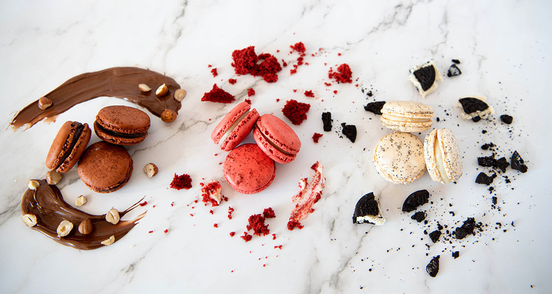 3 Nutella macarons, 3 Red Velvet macarons, and 3 Cookies & Cream macarons are placed horizontally over a marble top.