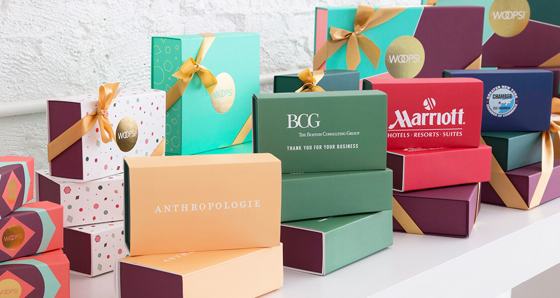 Multiple macaron boxes with customized sleeves are one beside the other on top of a white table.