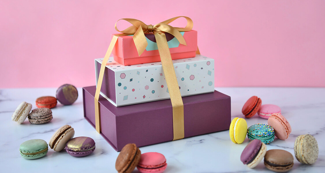 A French macaron stack with a ribbon on top is surrounded by assorted French macarons.