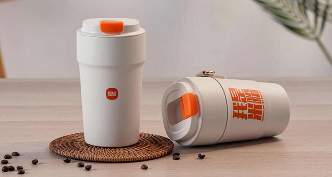 Two custom Xiaomi coffee cups have coffee beans to their left.