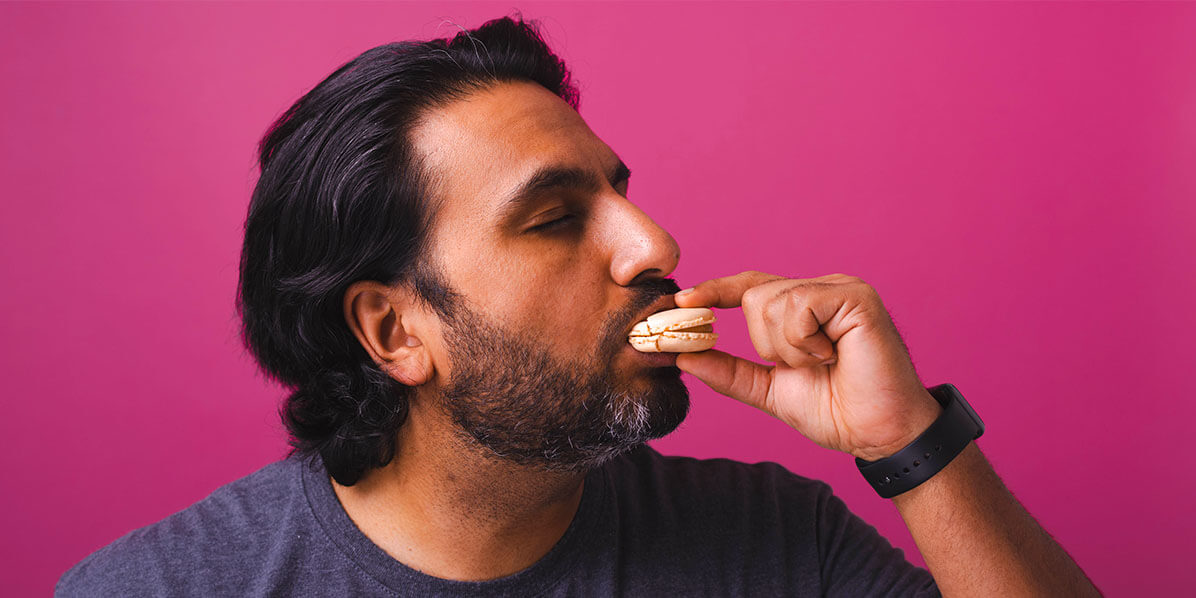 A man with dark hair is delightfully eating a Caramel Fleur de Sel French macaron.