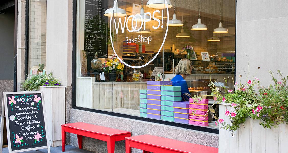 The front of a Woops! Bakeshop has numerous French macaron boxes on its front window.