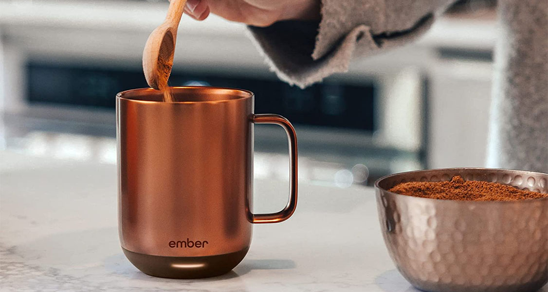 A female hand is putting some coffee into a bronze-colored mug.
