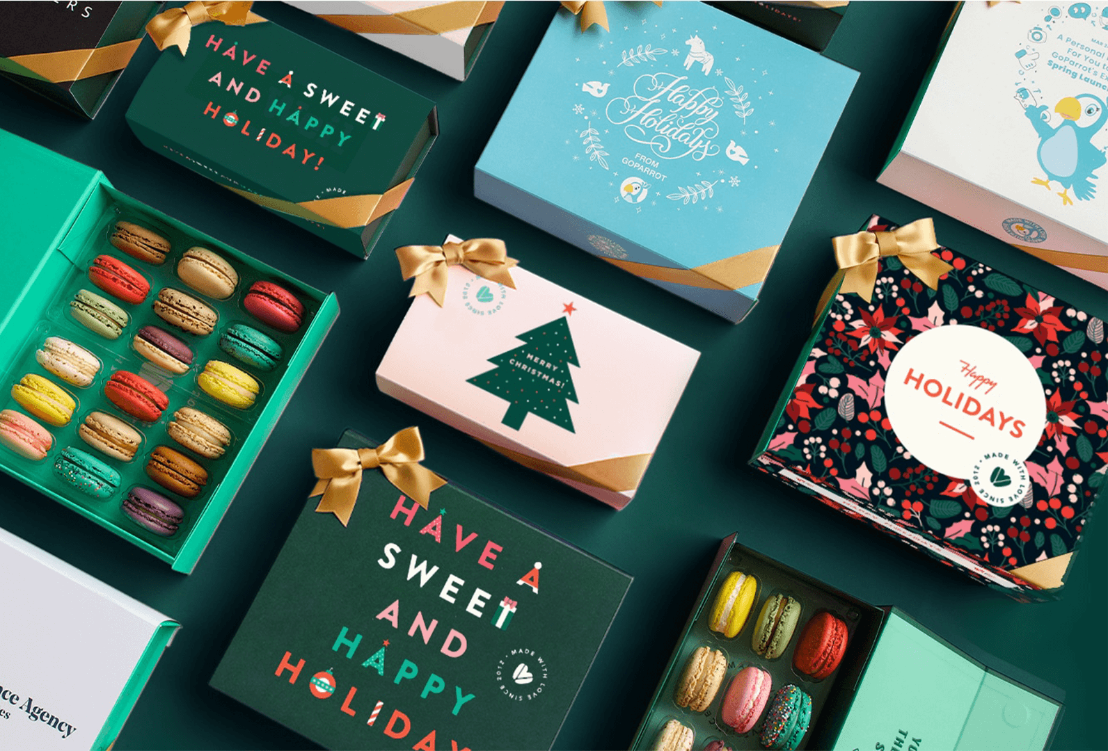 A box full of assorted French macarons has a French macaron box with a customized holiday sleeve and a customized greeting card to its left