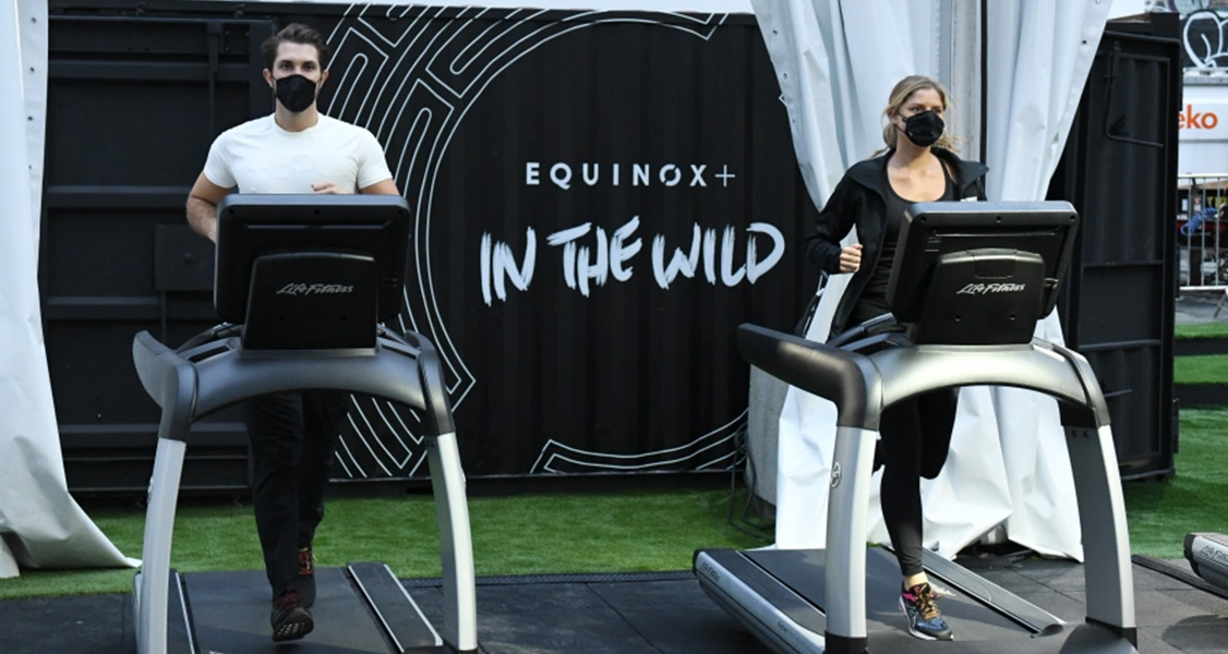A man and woman are running on two treadmills in an open space.