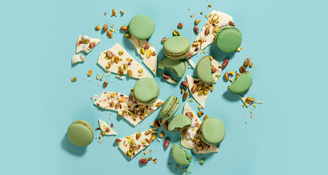 Several Pistachio French macarons are surrounded by white chocolate and pistachios.