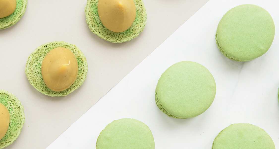 Several Pistachio French macaron shells laying on one side and on the other more shells with ganache on top.