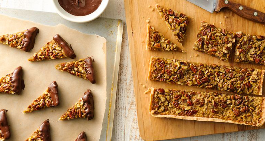 Pecan pie bars on a cutting board with chocolate to dip them