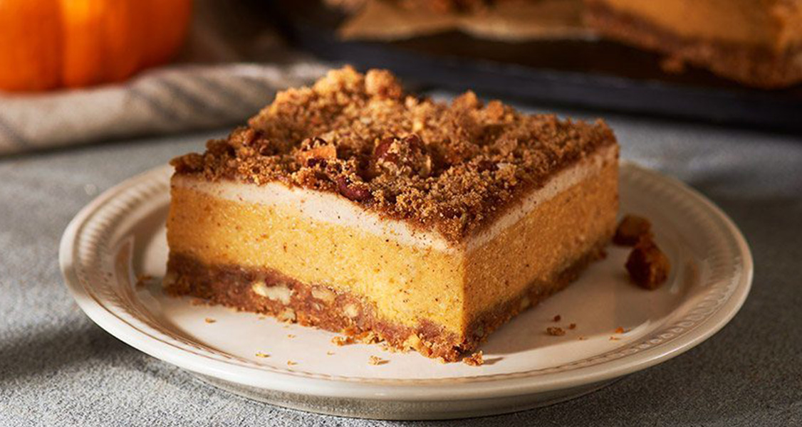 Pumpkin Cheesecake Squares on a plate with a small pumpkin in the back