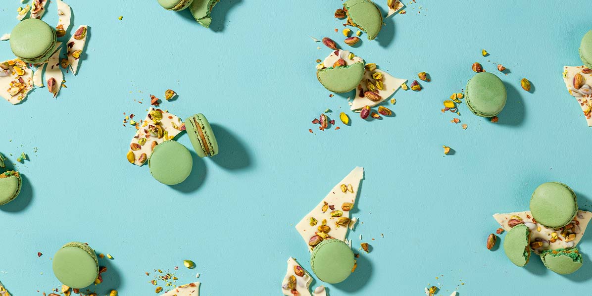 Several Pistachio French macarons are surrounded by white chocolate and pistachios.