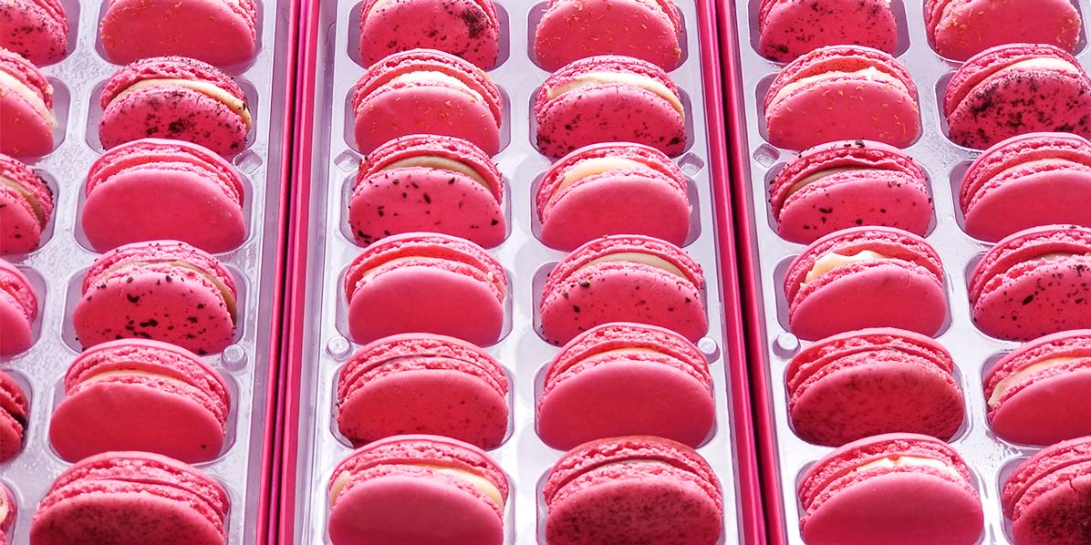 Several Woops! boxes full of pink dyed French macarons with assorted flavors.