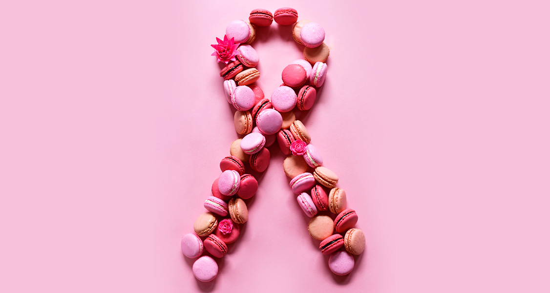 Several assorted French macarons are in a Breast Cancer Awareness-shaped ribbon.