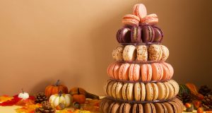 A French macaron pyramid with assorted flavors is surrounded by decorative pumpkins and paper leaves.