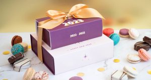 A stack of macaron boxes with New Year’s sleeves is surrounded by macarons and alfajores. 