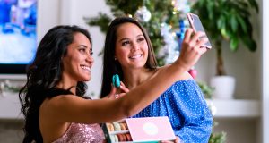 Two smiling women are taking a selfie while holding a French macaron box.