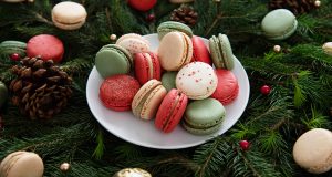 A plate full of macarons is surrounded by assorted macarons and holiday ornaments.