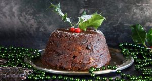 Christmas pudding on a table with green Christmas beads from https://www.glutenfreealchemist.com/traditional-gluten-free-christmas-pudding-recipe-figgy-pudding/