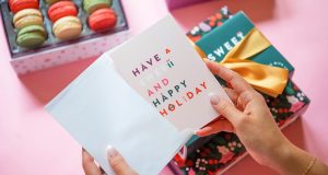 A pair of female hands open a Christmas card in front of boxes of macarons